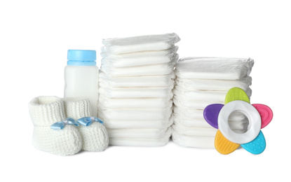 Photo of Disposable diapers, child's booties, teether and bottle on white background