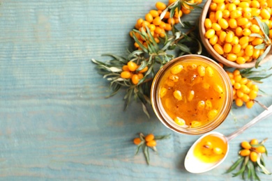 Photo of Delicious sea buckthorn jam and fresh berries on blue wooden table, flat lay. Space for text