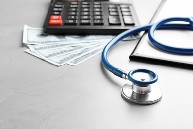 Stethoscope with money, clipboard and calculator on grey table, closeup. Medical insurance concept