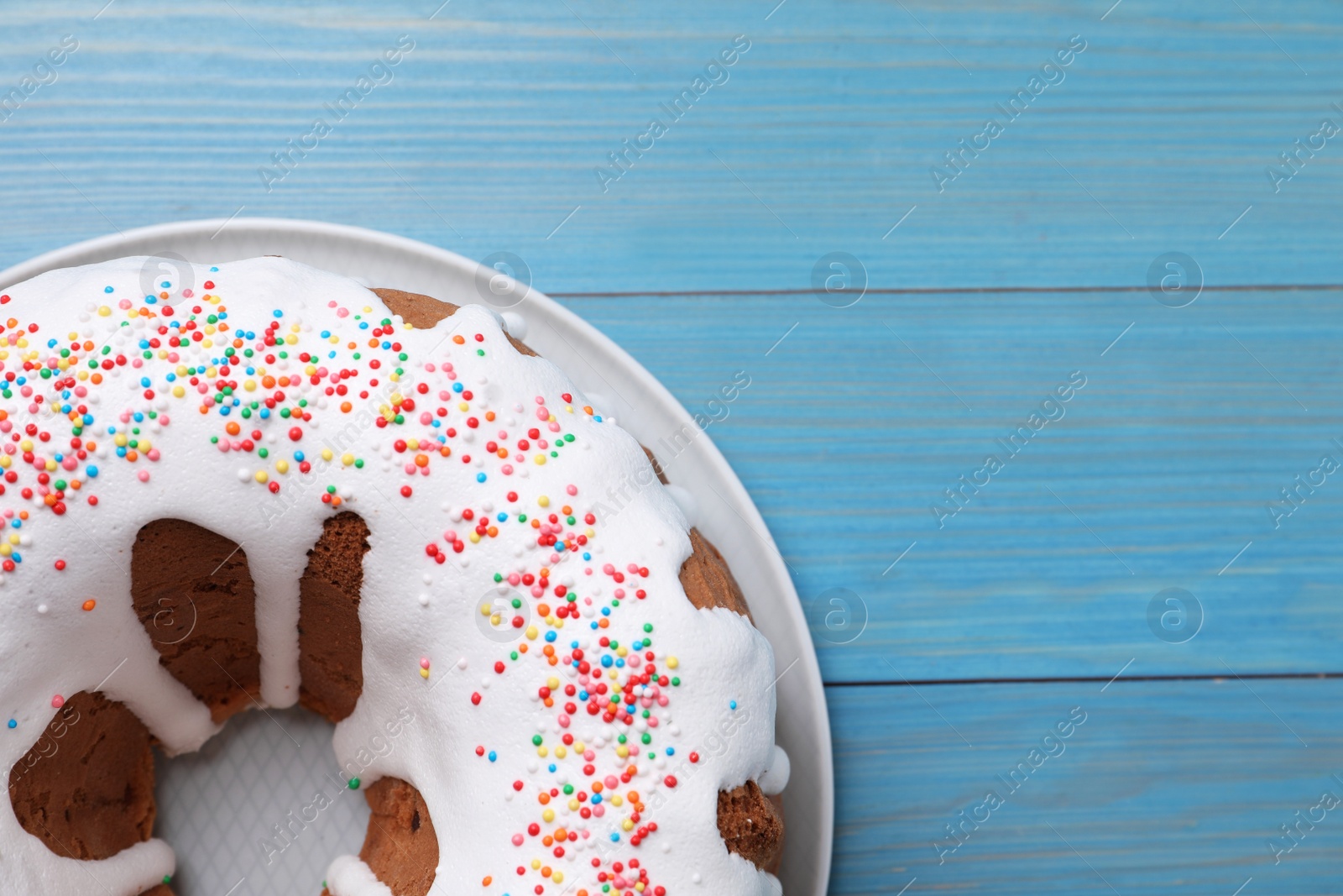 Photo of Glazed Easter cake with sprinkles on light blue wooden table, top view. Space for text