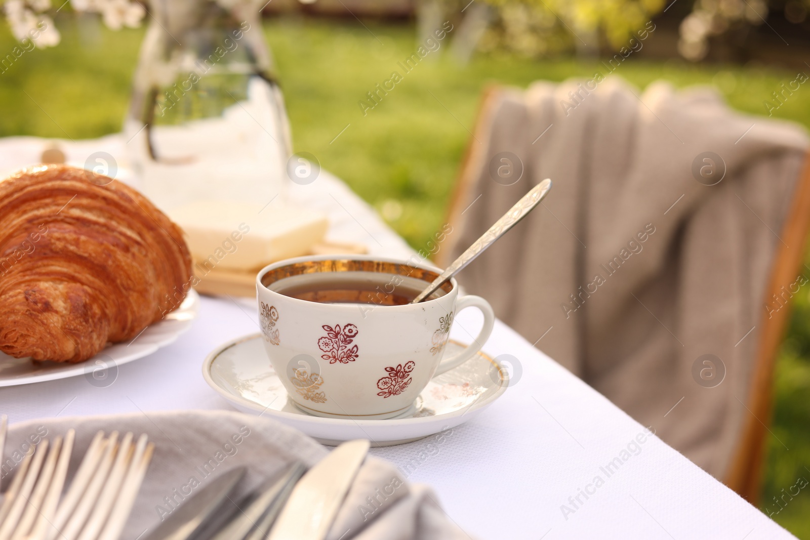 Photo of Stylish table setting with beautiful spring flowers, tea and croissants in garden