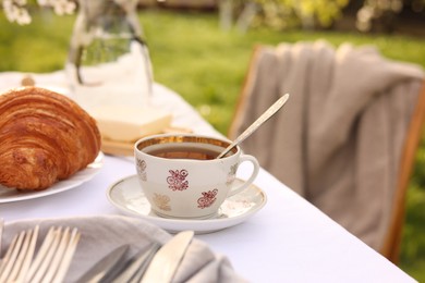 Stylish table setting with beautiful spring flowers, tea and croissants in garden