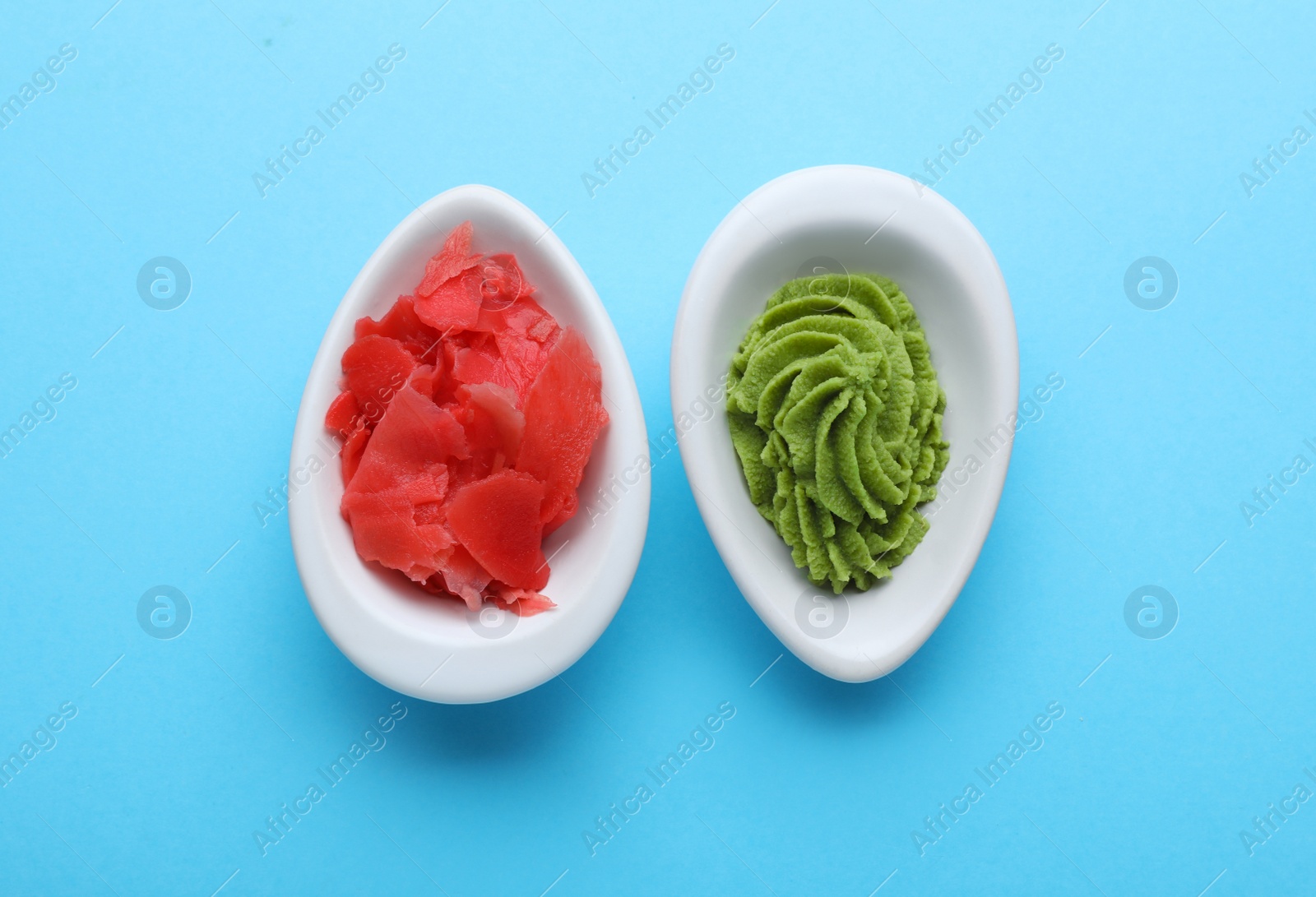 Photo of Bowls with swirl of wasabi paste and pickled ginger on light blue background, flat lay