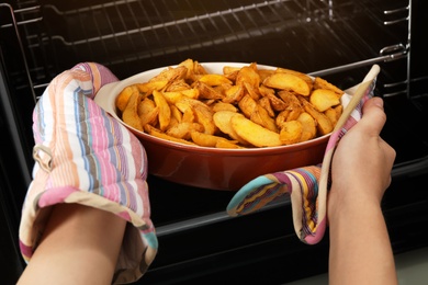 Photo of Woman taking hot roasted potatoes out of oven, closeup