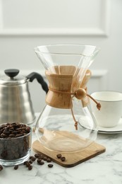Empty glass chemex coffeemaker and beans on white marble table
