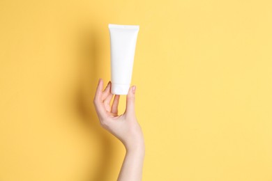 Photo of Woman holding tube of cream on yellow background, closeup. Space for text