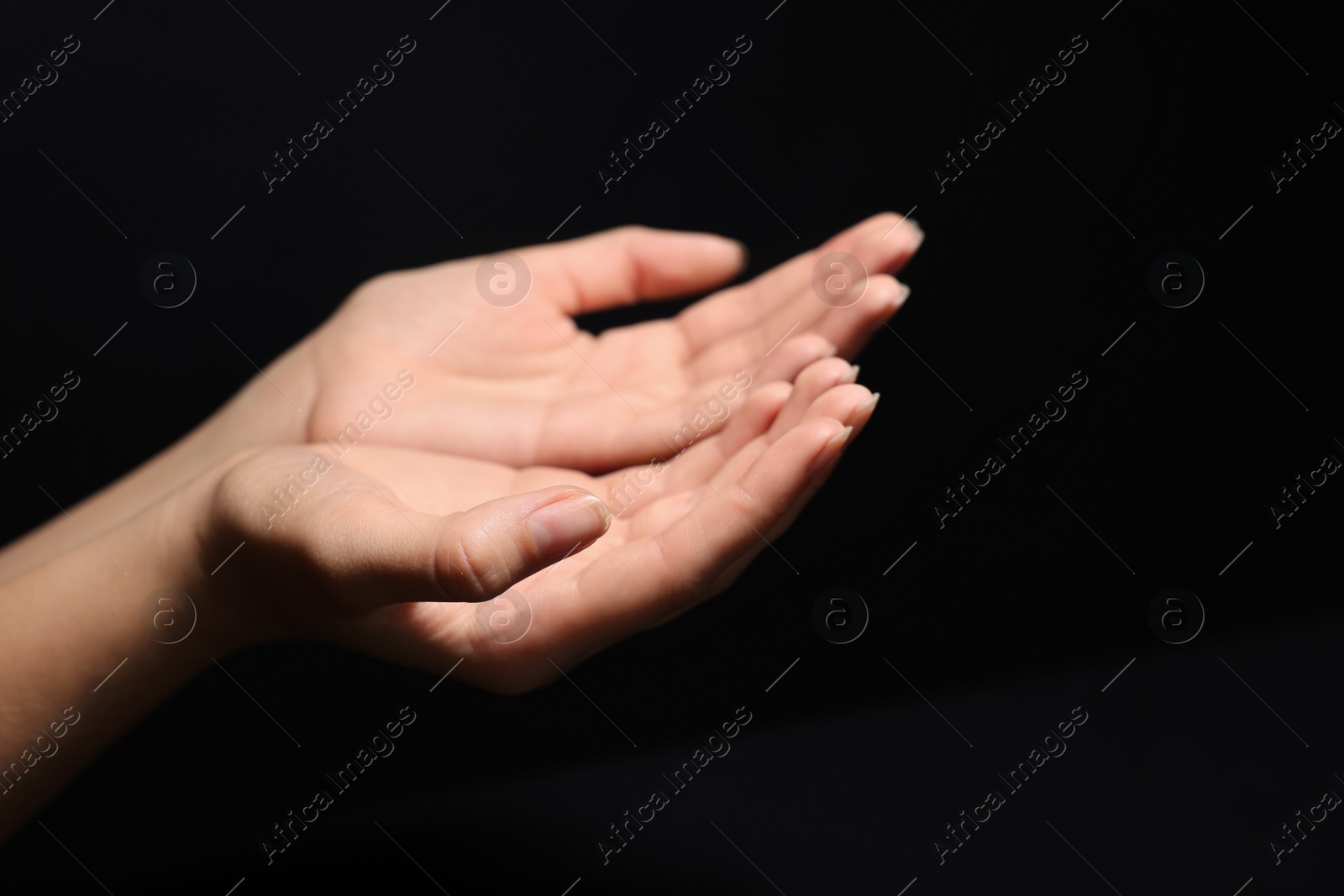 Photo of Woman stretching hands towards light in darkness, closeup