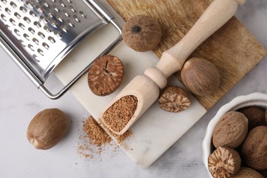 Photo of Scoop with grated nutmeg, seeds and grater on white marble table, flat lay
