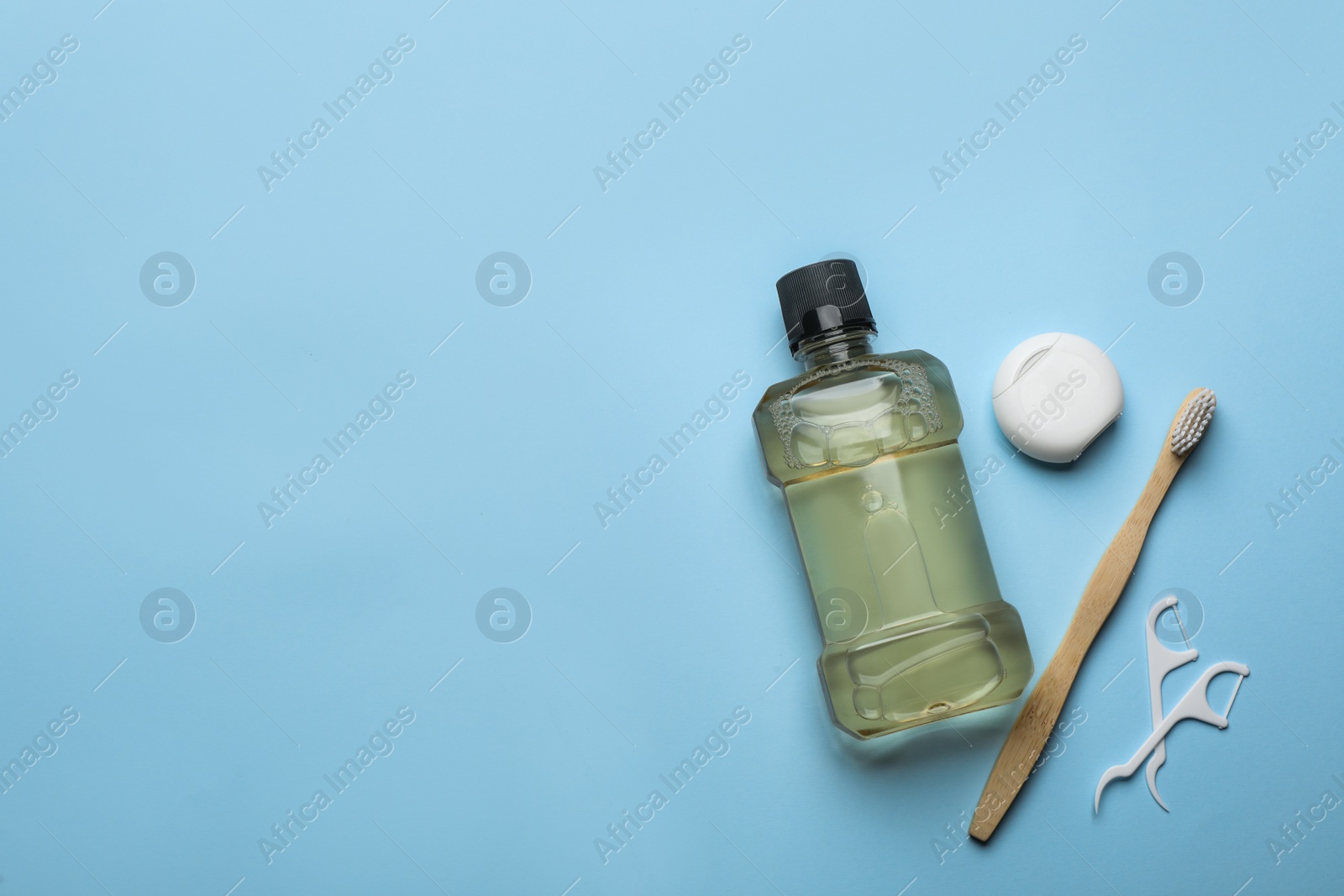 Photo of Mouthwash, toothbrush and dental floss on light blue background, flat lay. Space for text