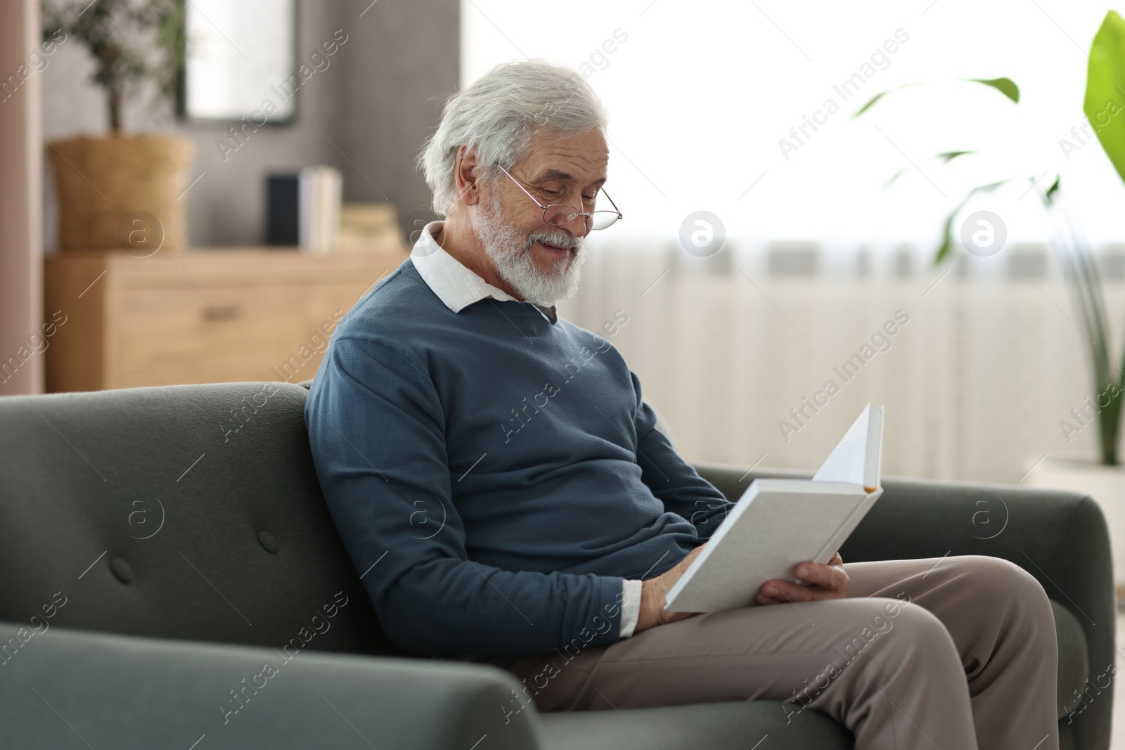 Photo of Portrait of happy grandpa reading book on sofa indoors