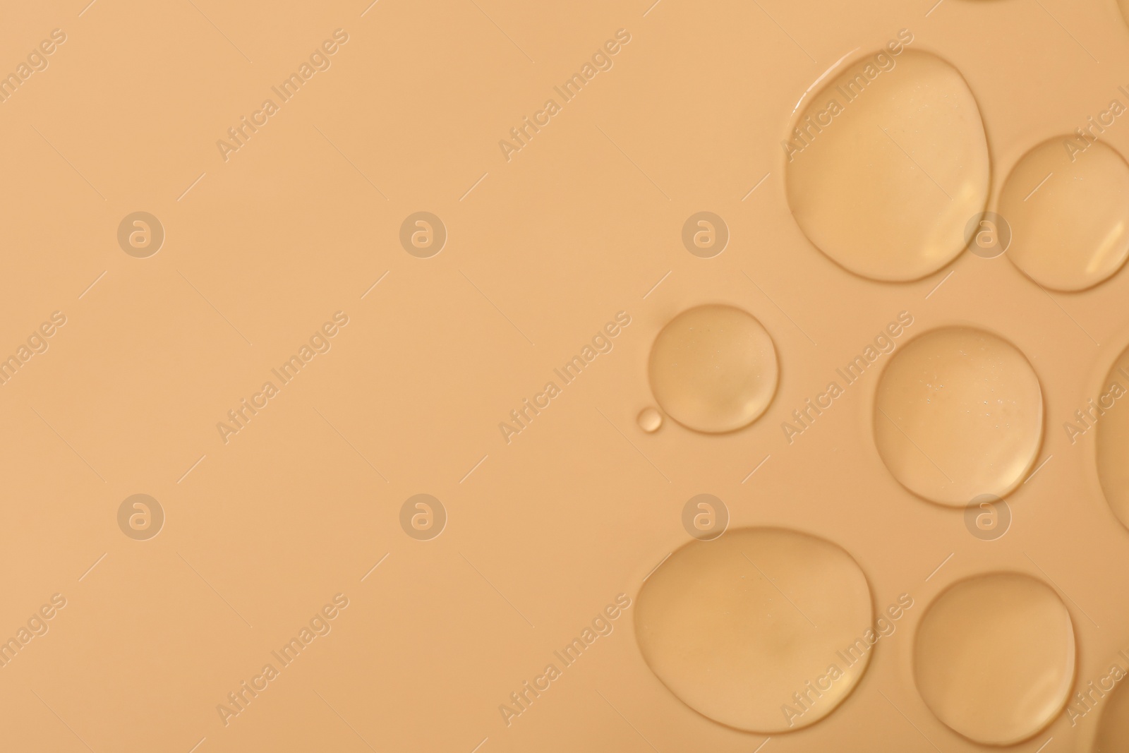 Photo of Drops of hydrophilic oil on beige background, flat lay. Space for text