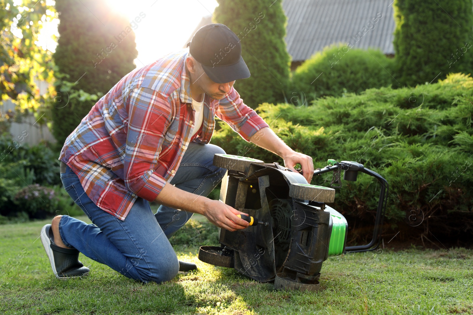 Photo of Man with screwdriver fixing lawn mower in garden on sunny day