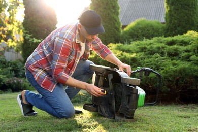 Photo of Man with screwdriver fixing lawn mower in garden on sunny day