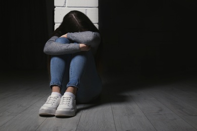Photo of Upset teenage girl sitting at column indoors. Space for text