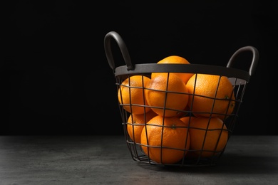 Photo of Basket with ripe oranges on table against dark background. Space for text