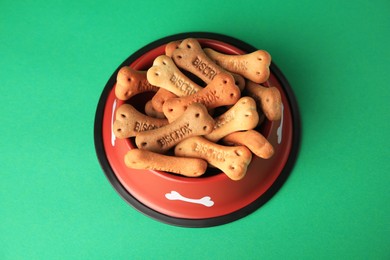 Bone shaped dog cookies in feeding bowl on green background, above view