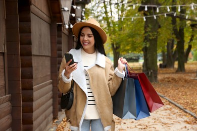 Special Promotion. Happy young woman with shopping bags and smartphone on city street