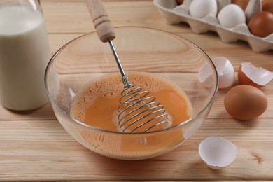 Making dough. Beaten eggs in bowl, shells and milk on wooden table, closeup