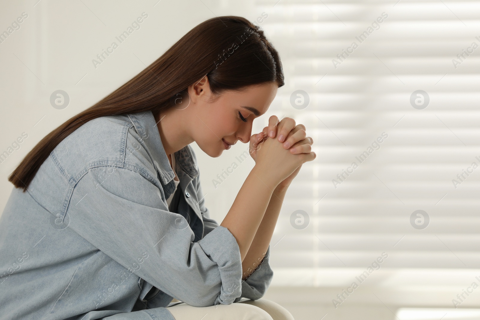 Photo of Religious young woman with clasped hands praying indoors