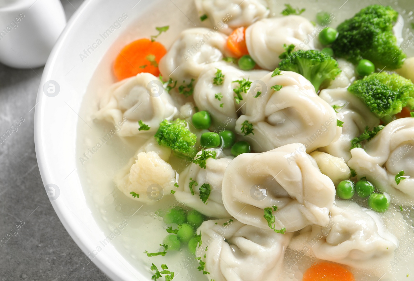 Photo of Bowl of tasty dumplings in broth on table, closeup