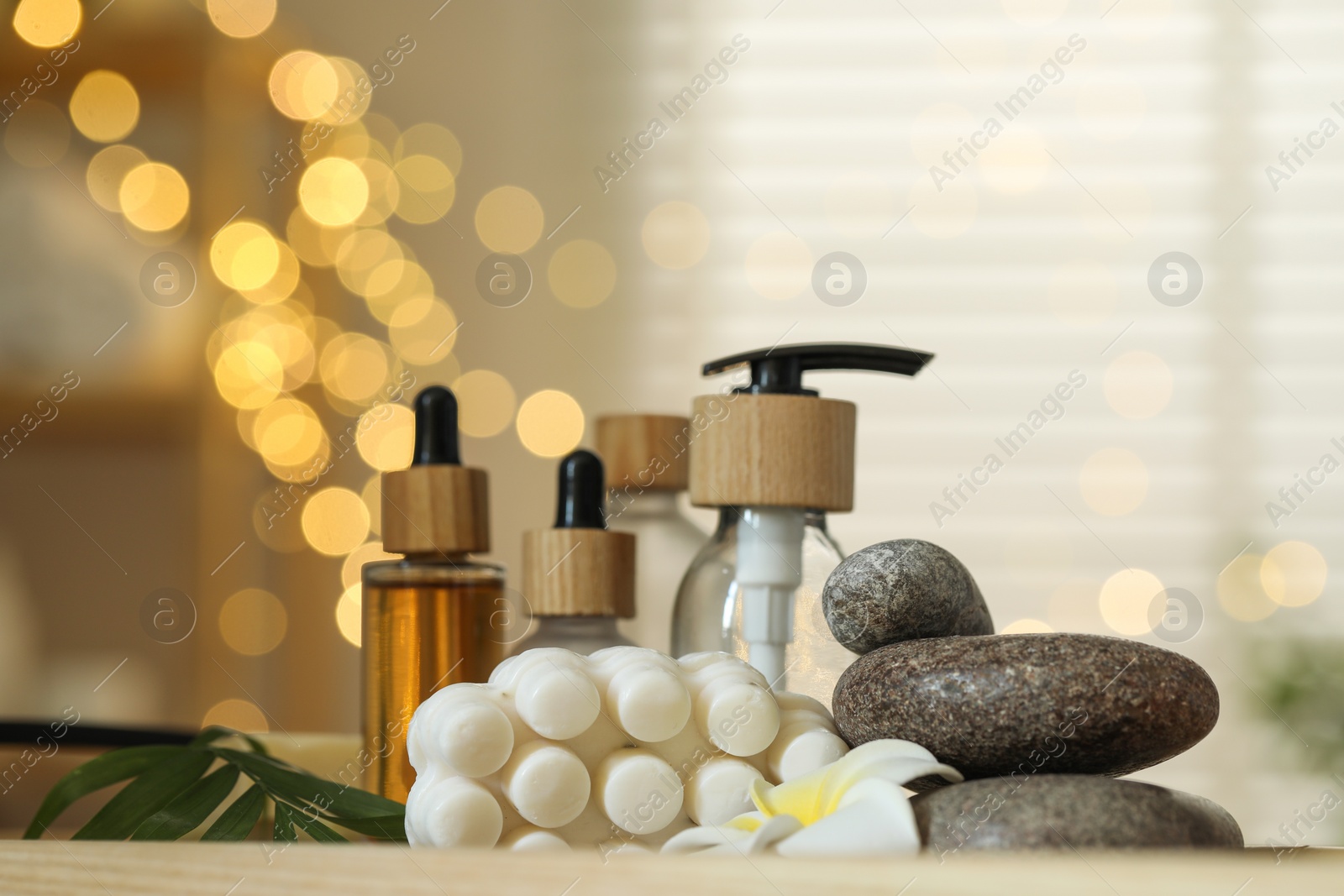 Photo of Composition with different spa products and plumeria flower on table indoors, bokeh effect