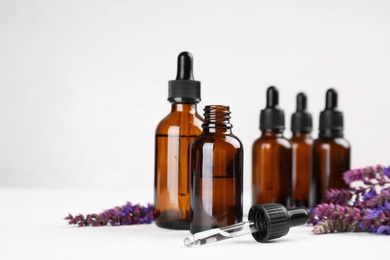 Photo of Bottles of sage essential oil and flowers on table, space for text