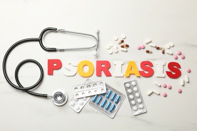 Photo of Word Psoriasis made of paper letters, stethoscope and pills on white table, flat lay