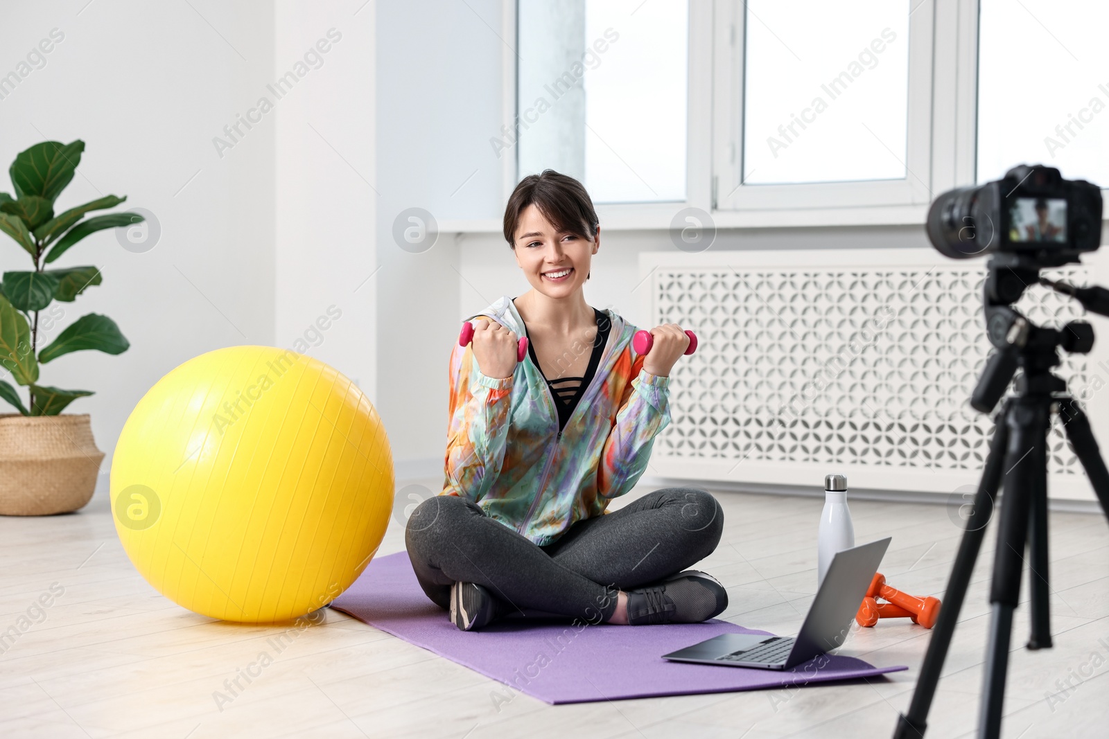 Photo of Happy sports blogger training with dumbbells while recording fitness lesson at home