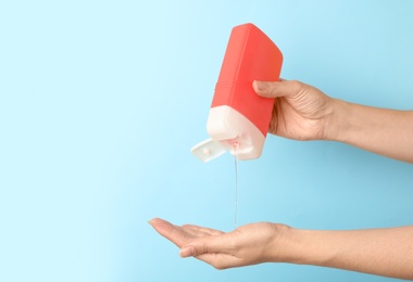 Image of Woman pouring personal hygiene product on hand against light blue background, closeup