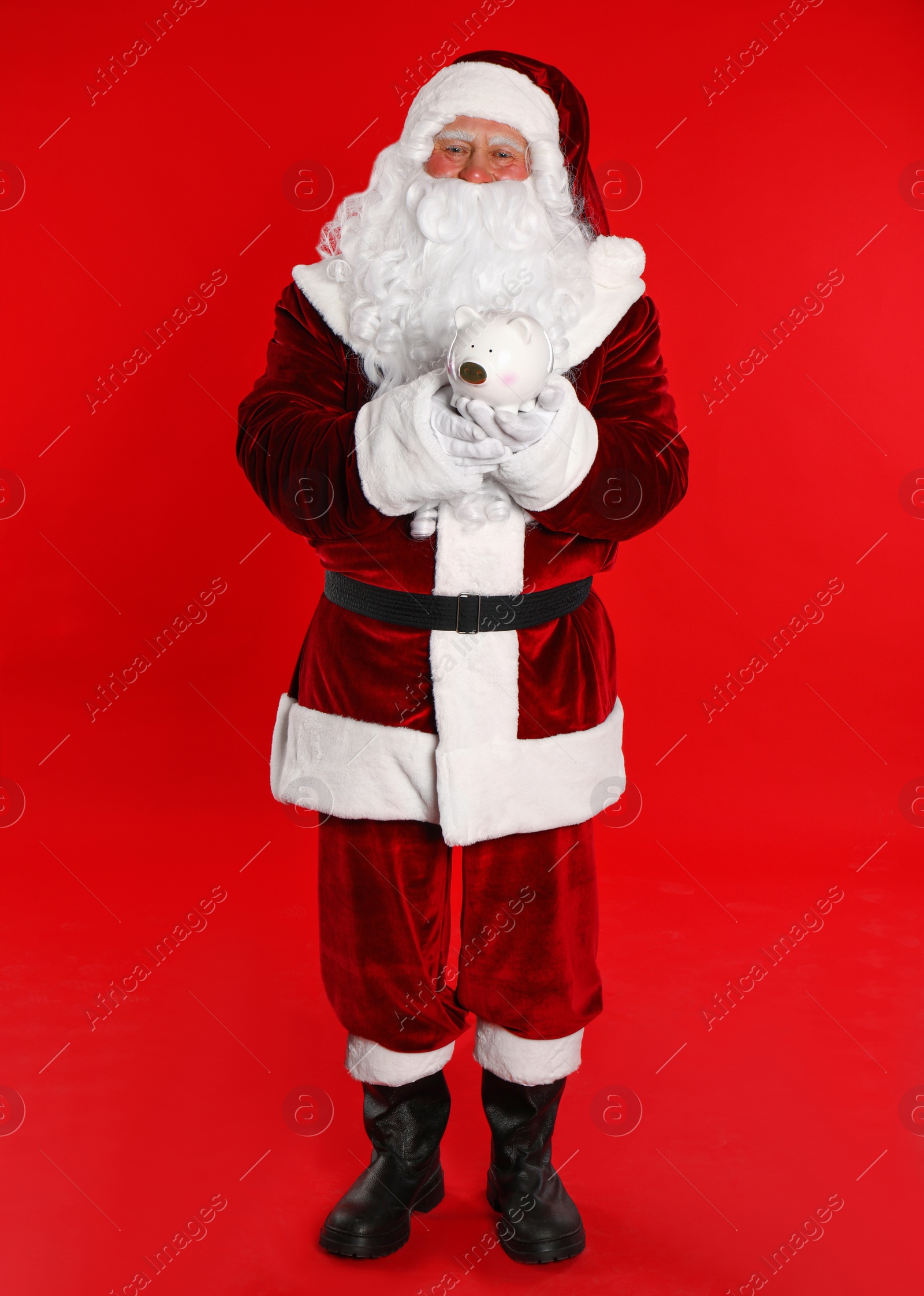 Photo of Santa Claus holding piggy bank on red background