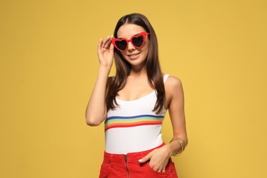 Portrait of beautiful young woman with heart shaped sunglasses on color background