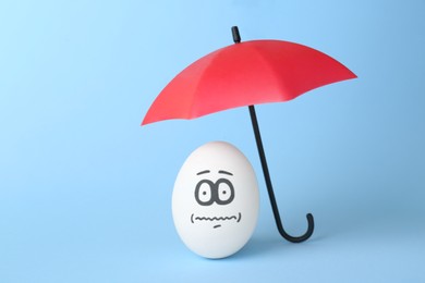 Photo of Egg with drawn frightened face and umbrella on turquoise background