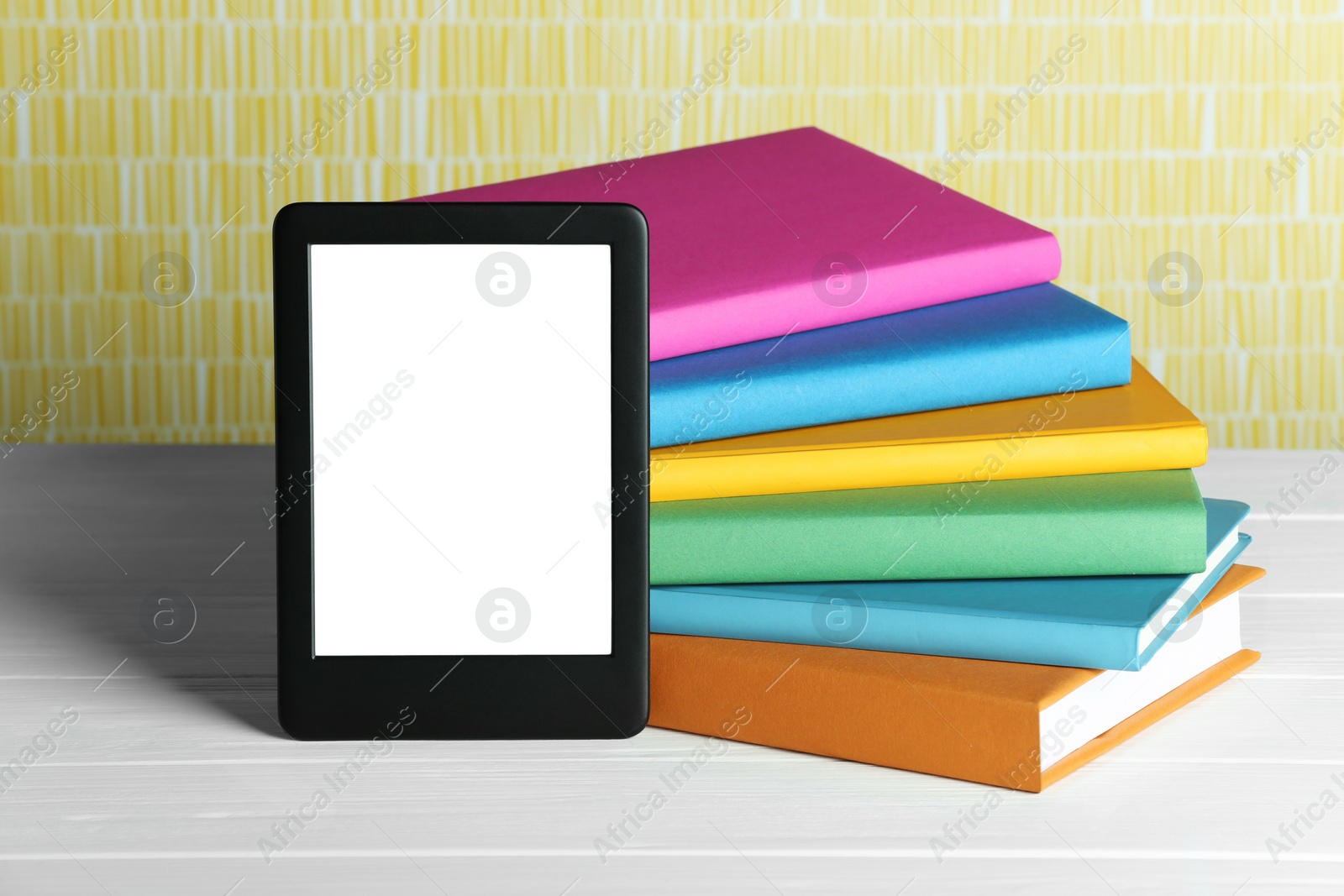 Photo of Portable e-book reader and stack of books on white wooden table