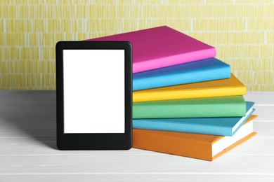 Photo of Portable e-book reader and stack of books on white wooden table
