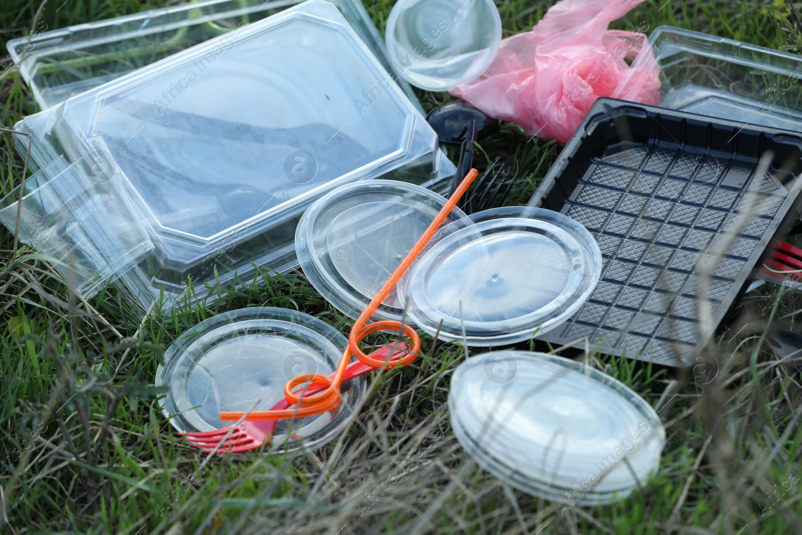 Photo of Used plastic tableware and bag on grass outdoors. Environmental pollution concept