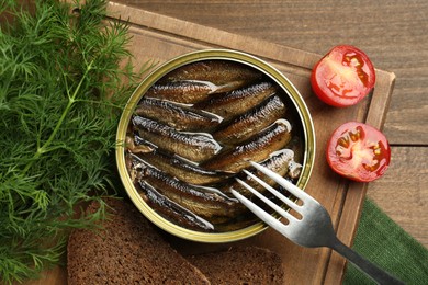 Tin can with tasty sprats and fork served on wooden table, flat lay