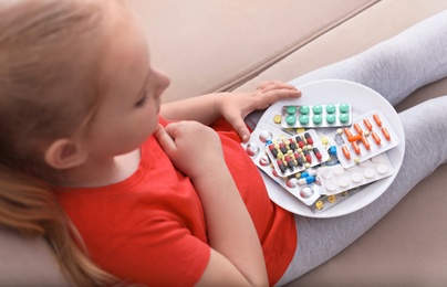 Photo of Little child with plate of different pills at home. Household danger