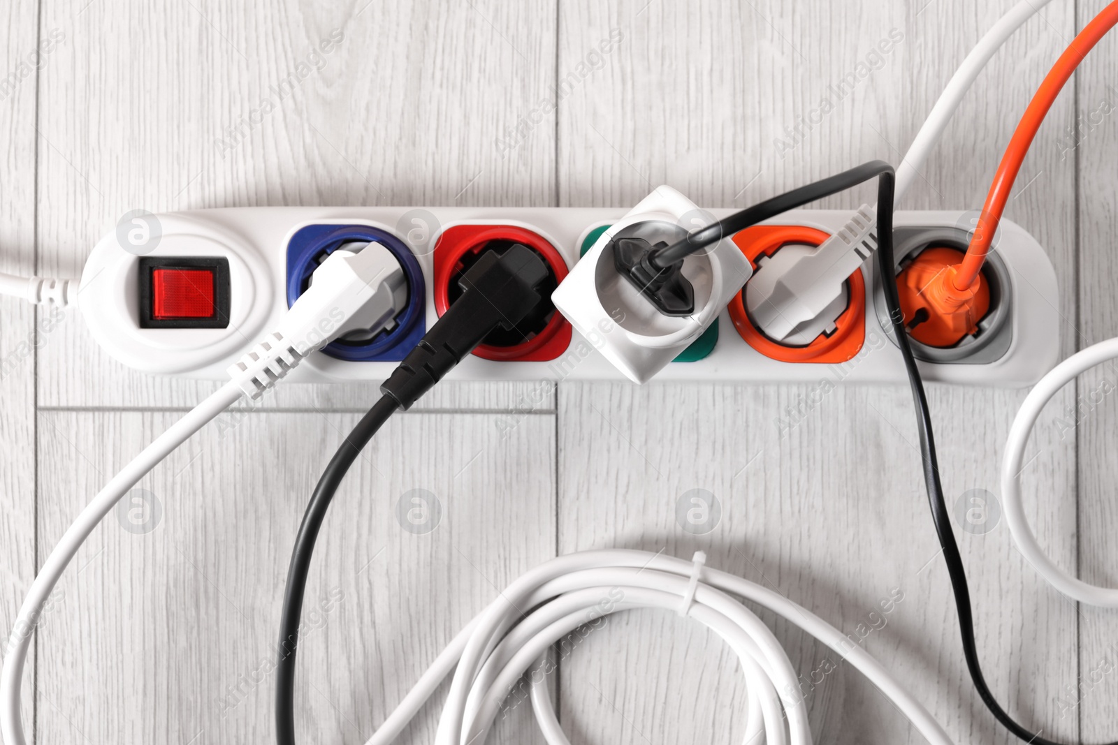 Photo of Power strip with different electrical plugs on white laminated floor, flat lay