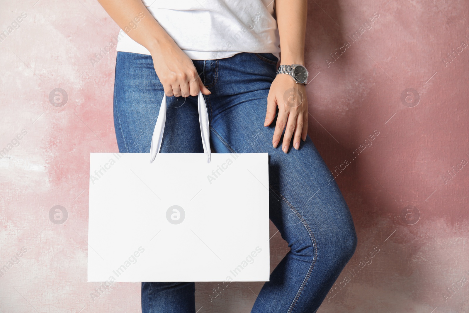 Photo of Woman holding mock-up of paper shopping bag on color background