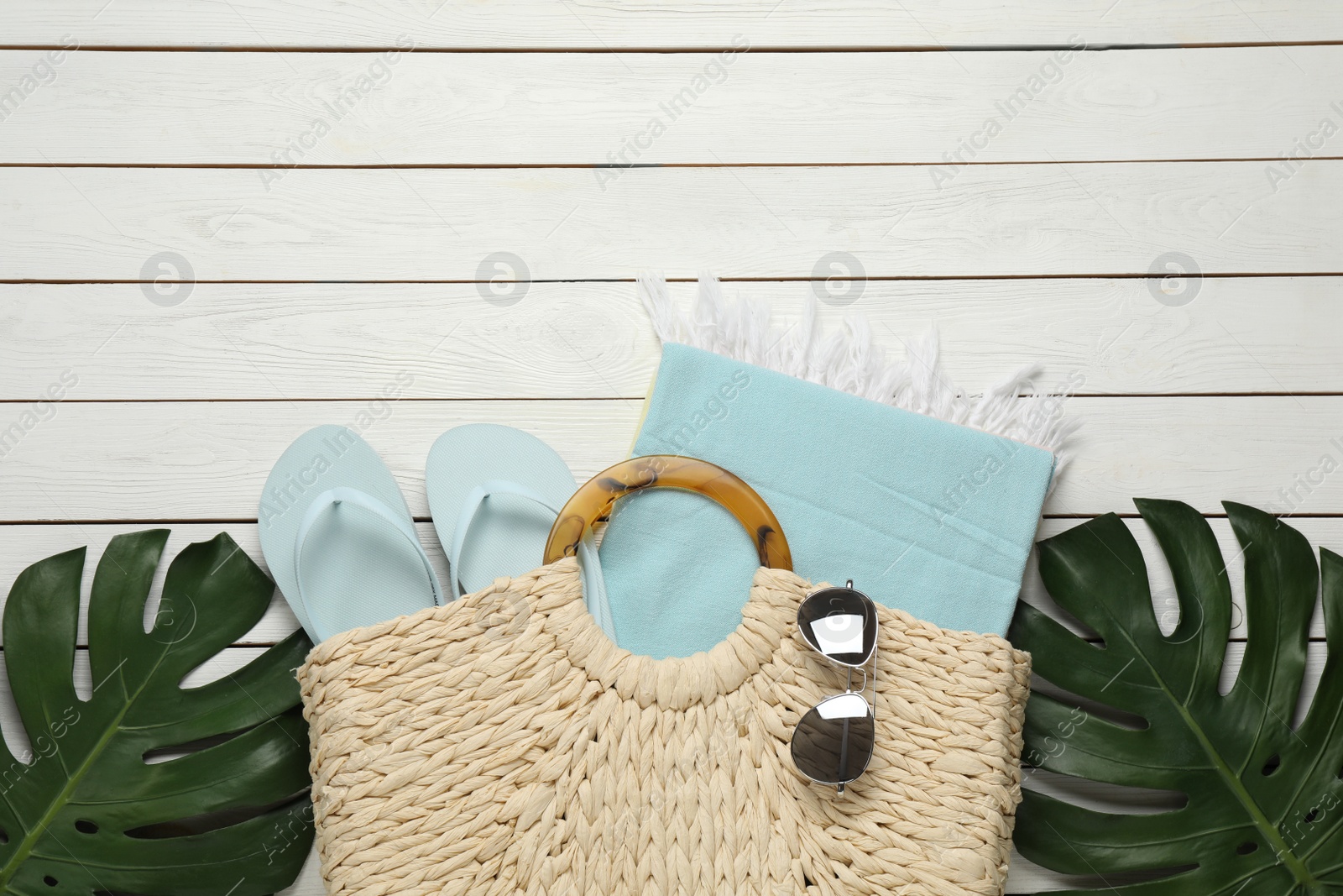 Photo of Beach bag with towel, flip flops and sunglasses on white wooden background, flat lay. Space for text