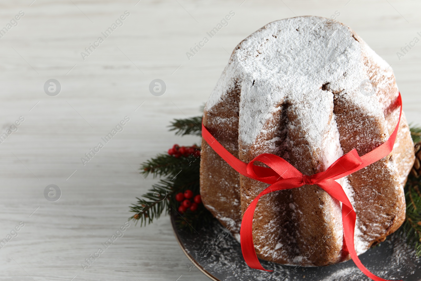 Photo of Delicious Pandoro cake with powdered sugar and red bow, Christmas decor on white wooden table, space for text. Traditional Italian pastry