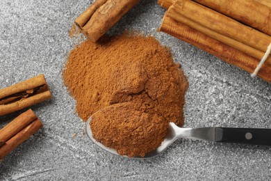 Spoon with cinnamon powder and sticks on grey table, flat lay