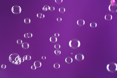 Photo of Beautiful transparent soap bubbles on purple background