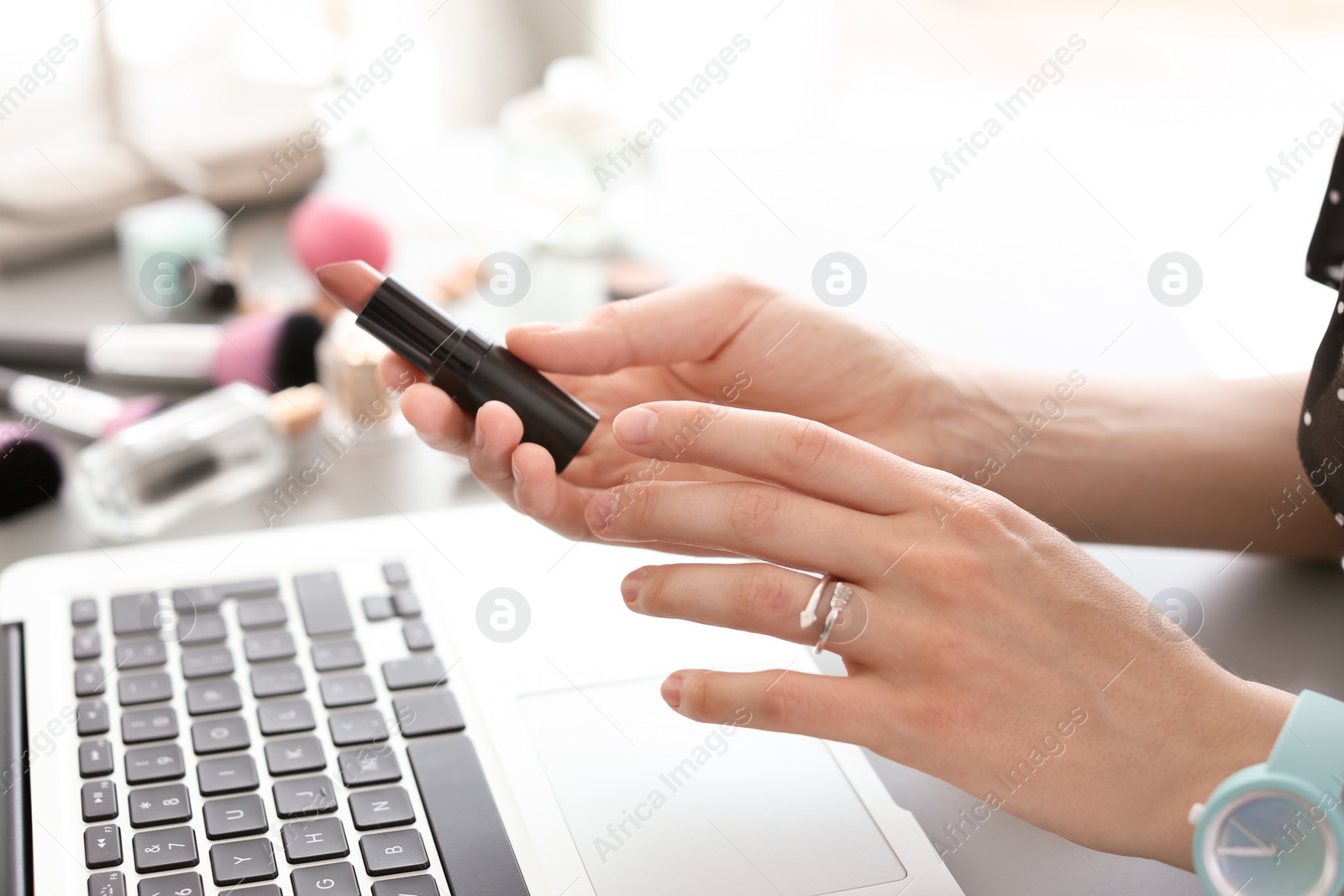 Photo of Young woman with makeup product using laptop at table. Beauty blogger