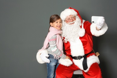 Authentic Santa Claus taking selfie with little girl on grey background