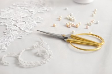 Photo of Pair of scissors, beautiful lace and beads on white table, closeup