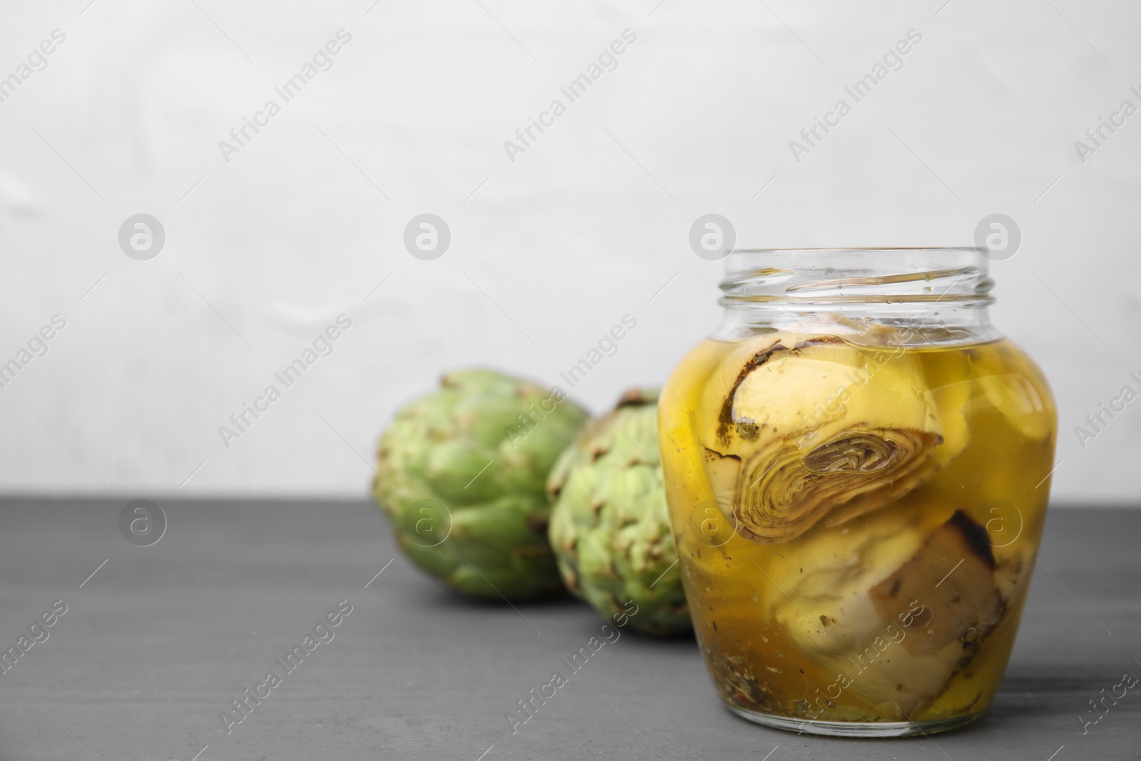 Photo of Pickled and fresh artichokes on grey wooden table. Space for text