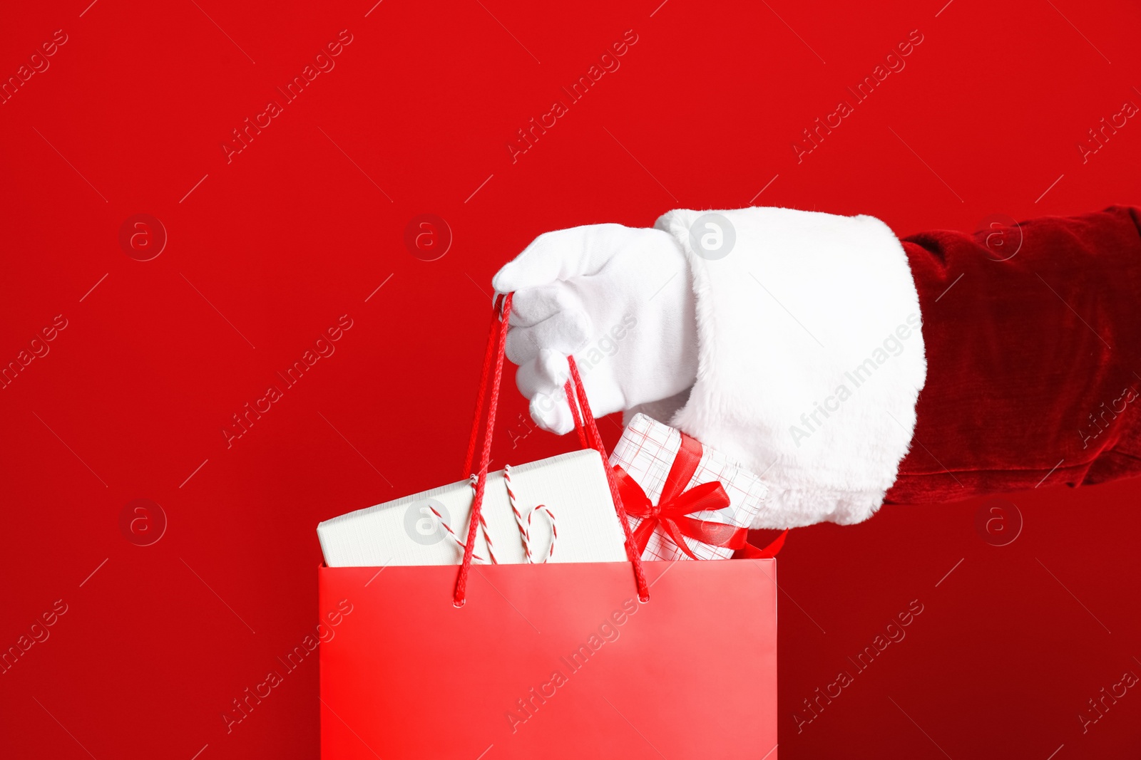 Photo of Santa holding paper bag with gift boxes on red background, closeup