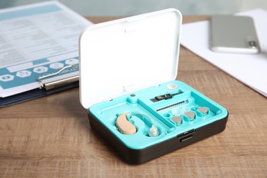 Box with hearing aid set on wooden table. Medical device