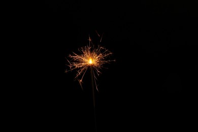 Photo of One burning sparkler stick on black background